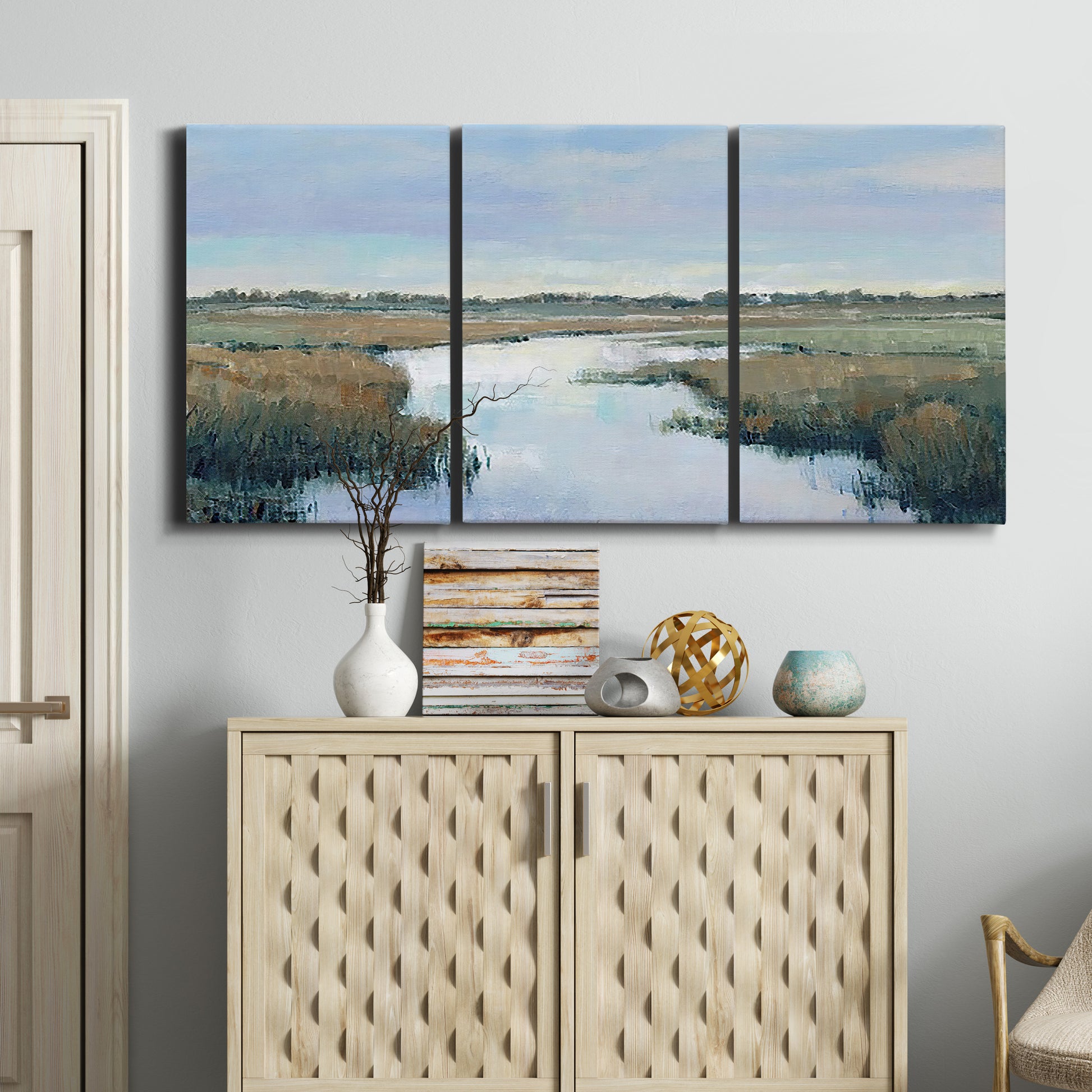 Three-panel canvas wall art featuring coastal plain with layered horizon, displayed above a cabinet in an entryway.