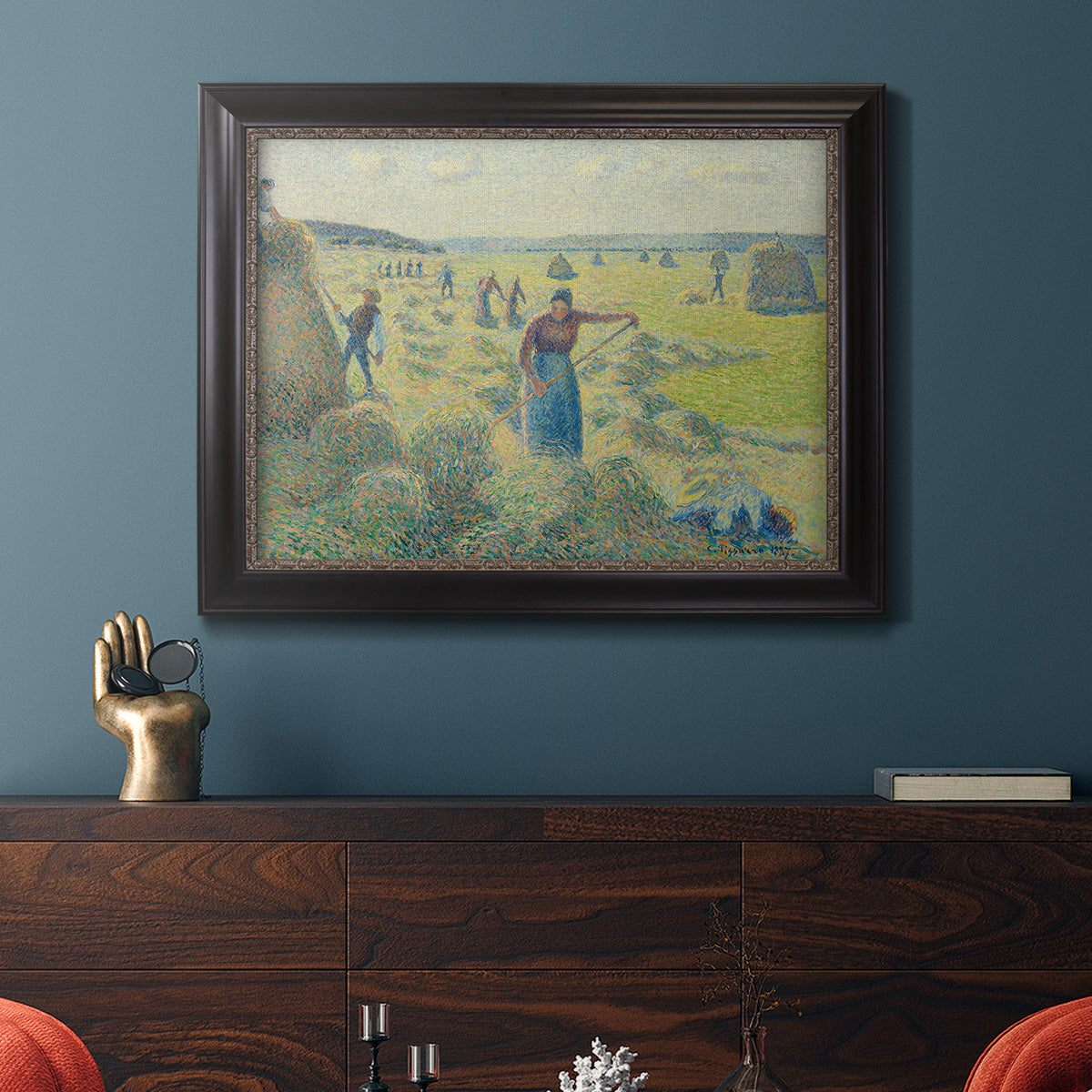 Impressionist rural hay harvest landscape by Camille Pissarro in an ornate black frame with gilded inner detail displayed in a dark-toned interior setting.