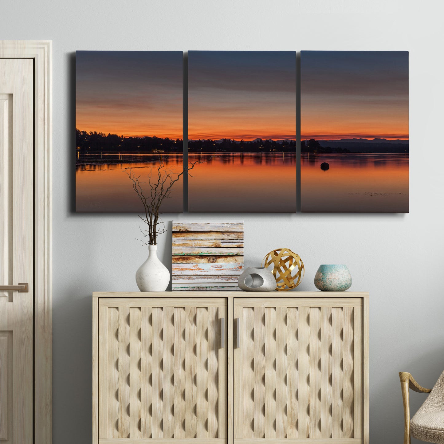 Three-panel canvas wall art featuring glowing sunset over water, displayed above a cabinet in an entryway.