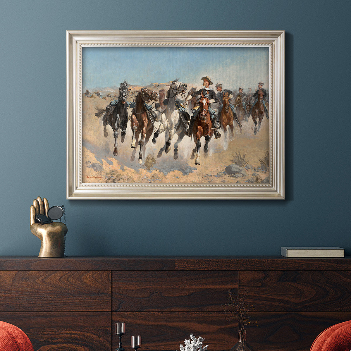 Impressionist western action scene by Frederic Remington in an ornate champagne frame displayed in a dark-toned interior setting.