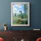Impressionist pastoral landscape with poppy fields by Claude Monet in an ornate weathered white frame displayed in a dark-toned interior setting.
