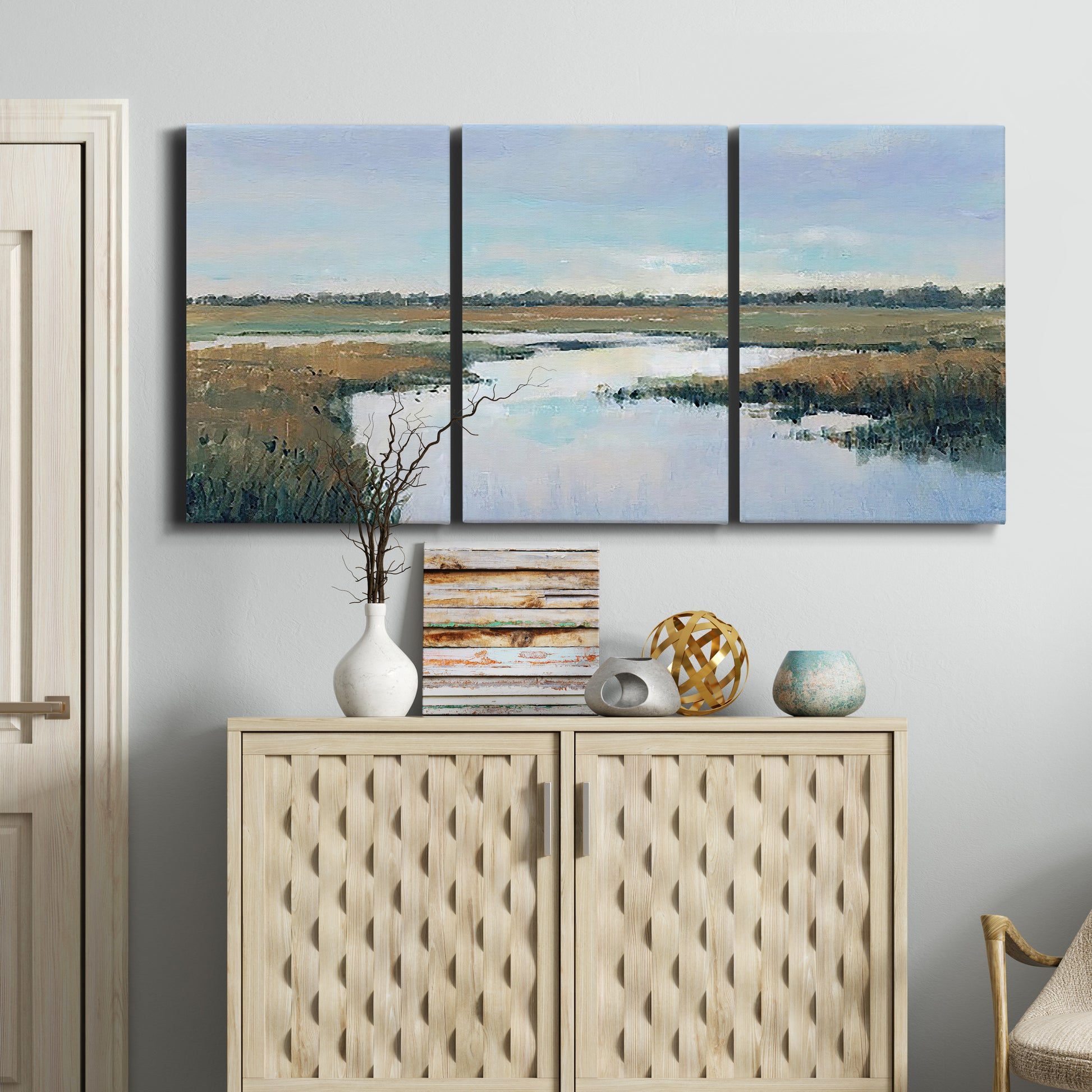 Three-panel canvas wall art featuring coastal plain meeting open water, displayed above a cabinet in an entryway.