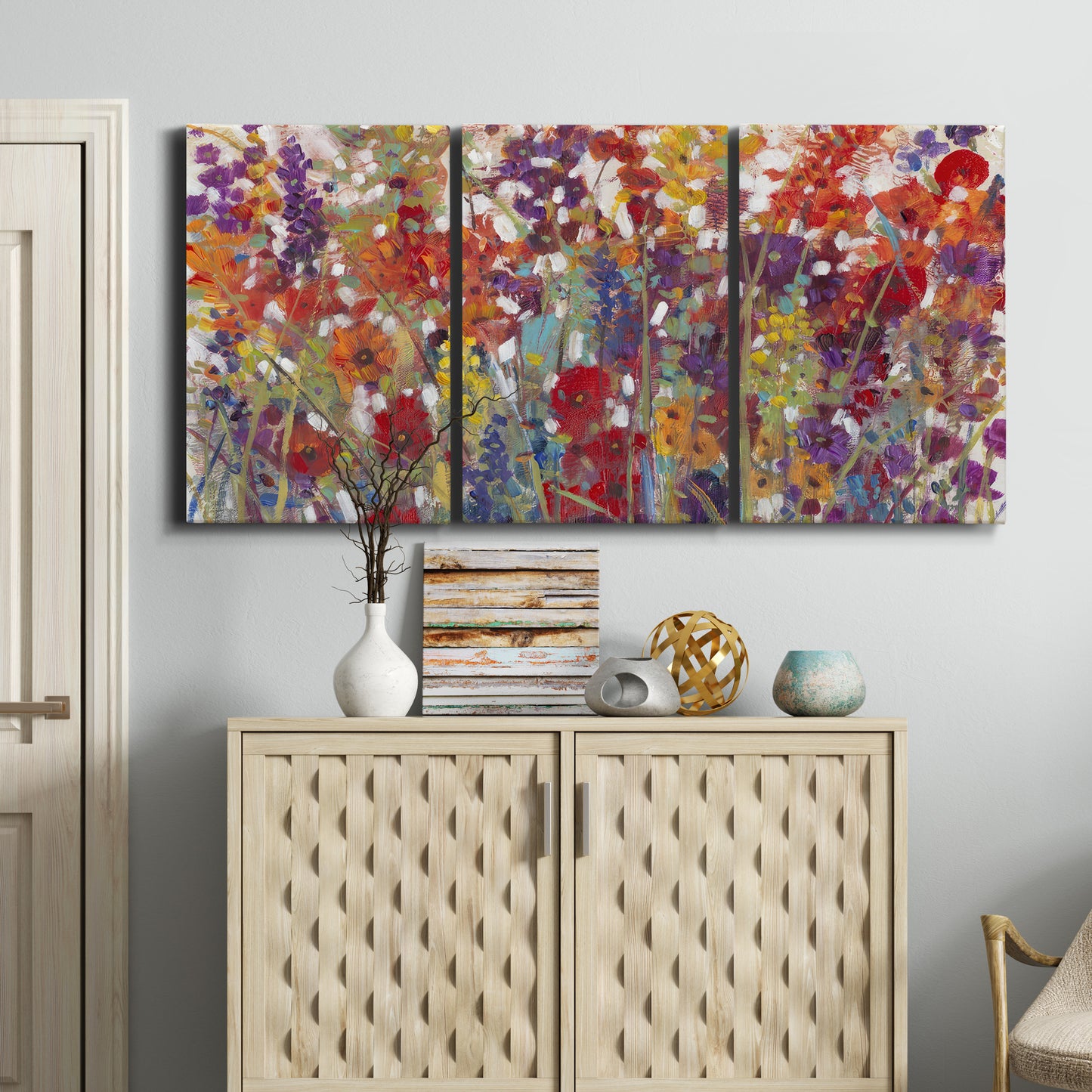 Three-panel canvas wall art featuring colorful floral arrangement, displayed above a cabinet in an entryway.