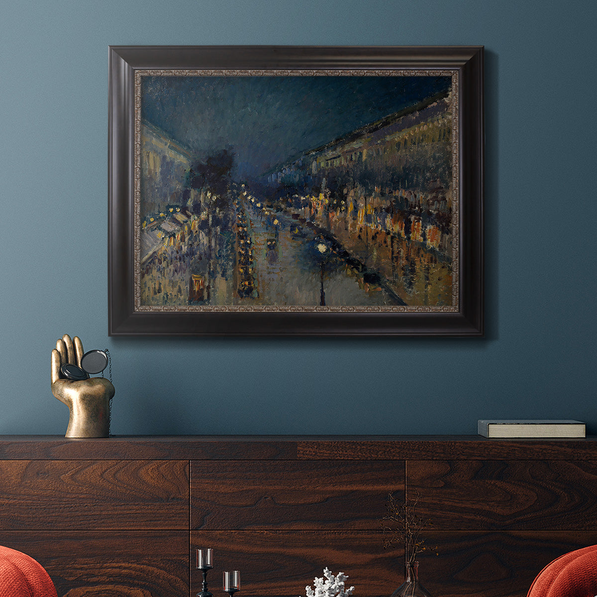 Impressionist nighttime Paris street scene by Camille Pissarro in an ornate black frame with gilded inner detail displayed in a dark-toned interior setting.