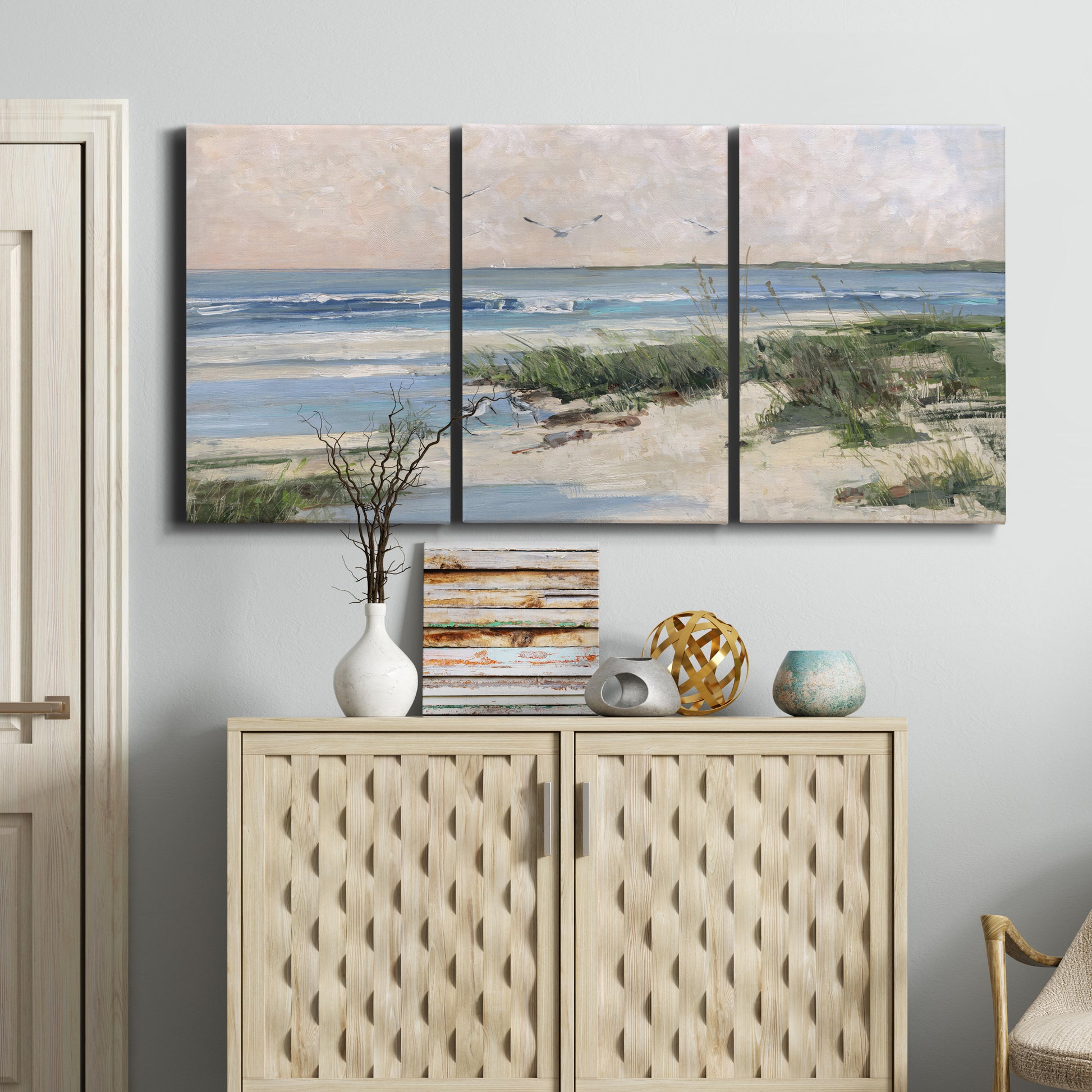 Three-panel canvas wall art featuring soft morning light over calm sea, displayed above a cabinet in an entryway.