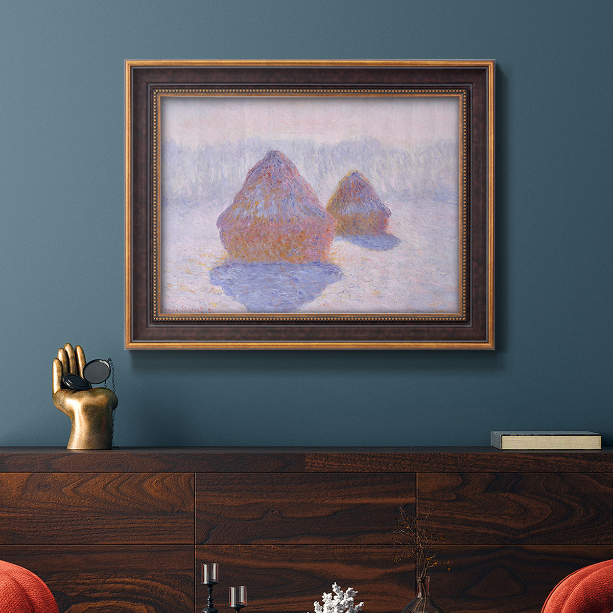 Impressionist winter haystack scene with sunlight by Claude Monet in an ornate bronzed mahogany wood frame displayed in a dark-toned interior setting.