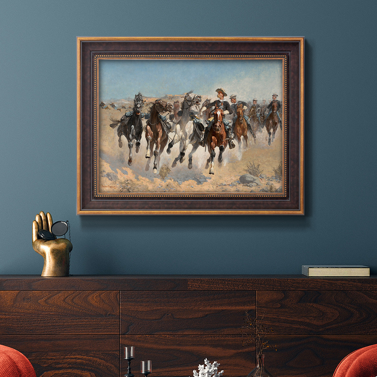 Impressionist western action scene by Frederic Remington in an ornate bronzed mahogany wood frame displayed in a dark-toned interior setting.