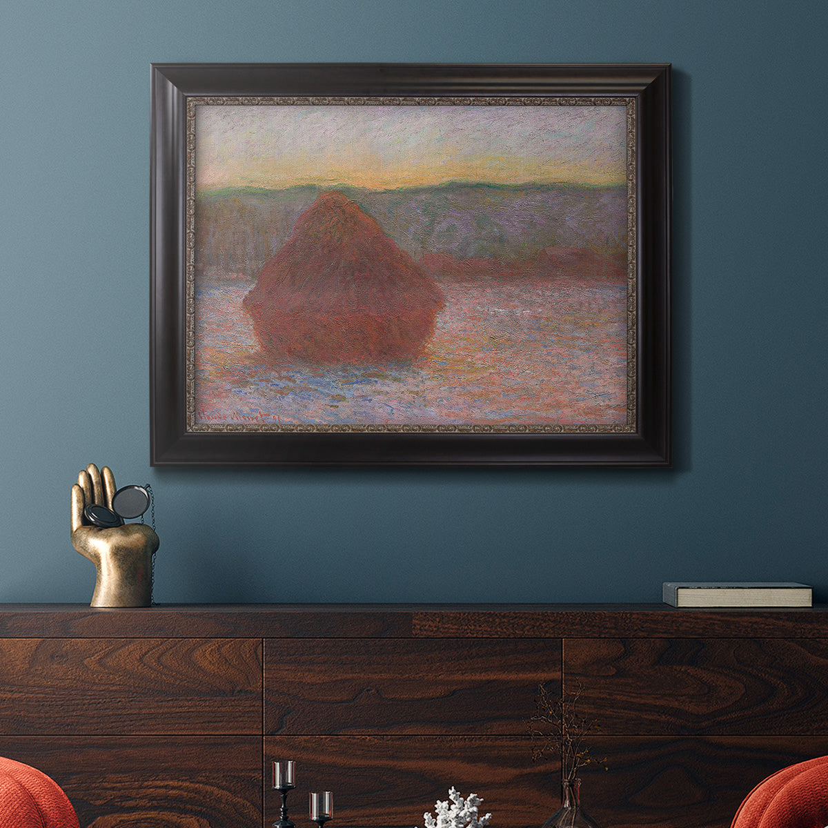 Impressionist haystack sunset scene in winter by Claude Monet in an ornate black frame with gilded inner detail displayed in a dark-toned interior setting.