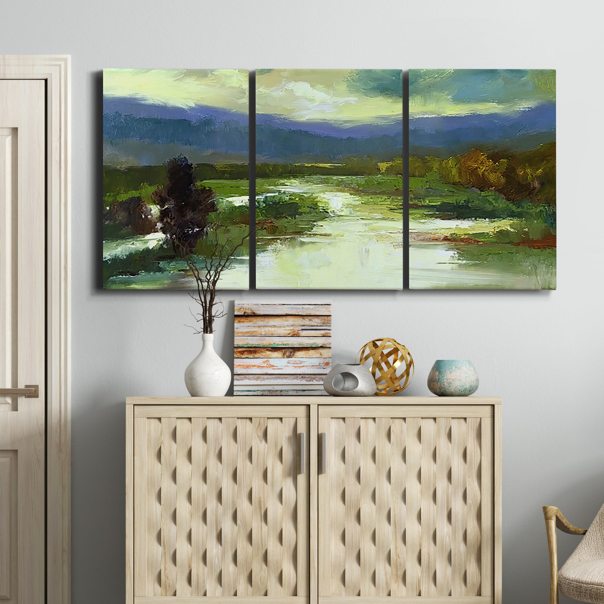 Three-panel canvas wall art featuring open meadow landscape with distant hills, displayed above a cabinet in an entryway.