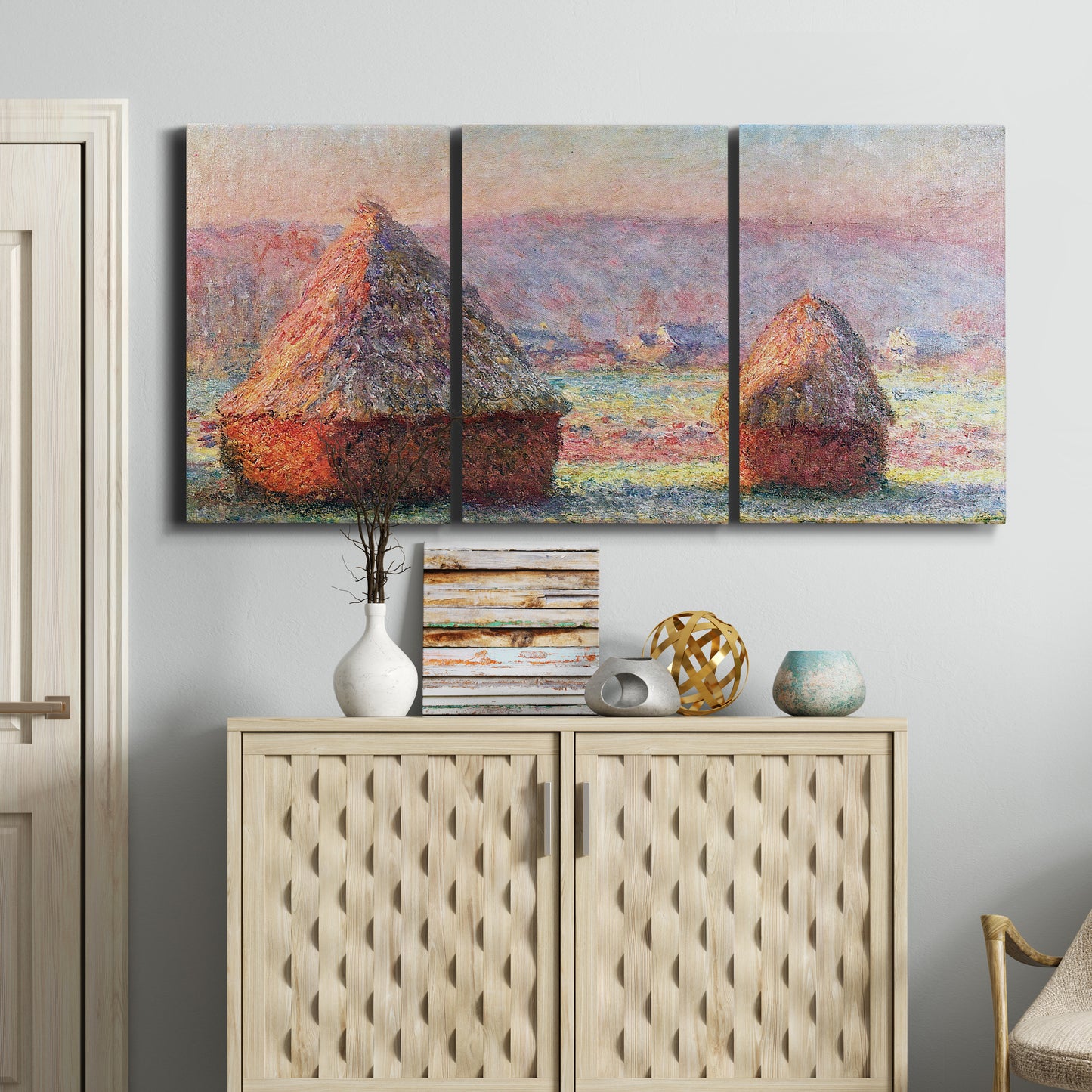 Three-panel canvas wall art featuring winter grainstacks glowing at sunset, displayed above a cabinet in an entryway.