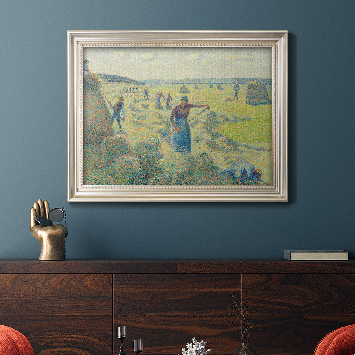 Impressionist rural hay harvest landscape by Camille Pissarro in an ornate champagne frame displayed in a dark-toned interior setting.