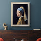 Iconic portrait of a girl wearing a pearl earring by Johannes Vermeer in an ornate champagne frame displayed in a dark-toned interior setting.