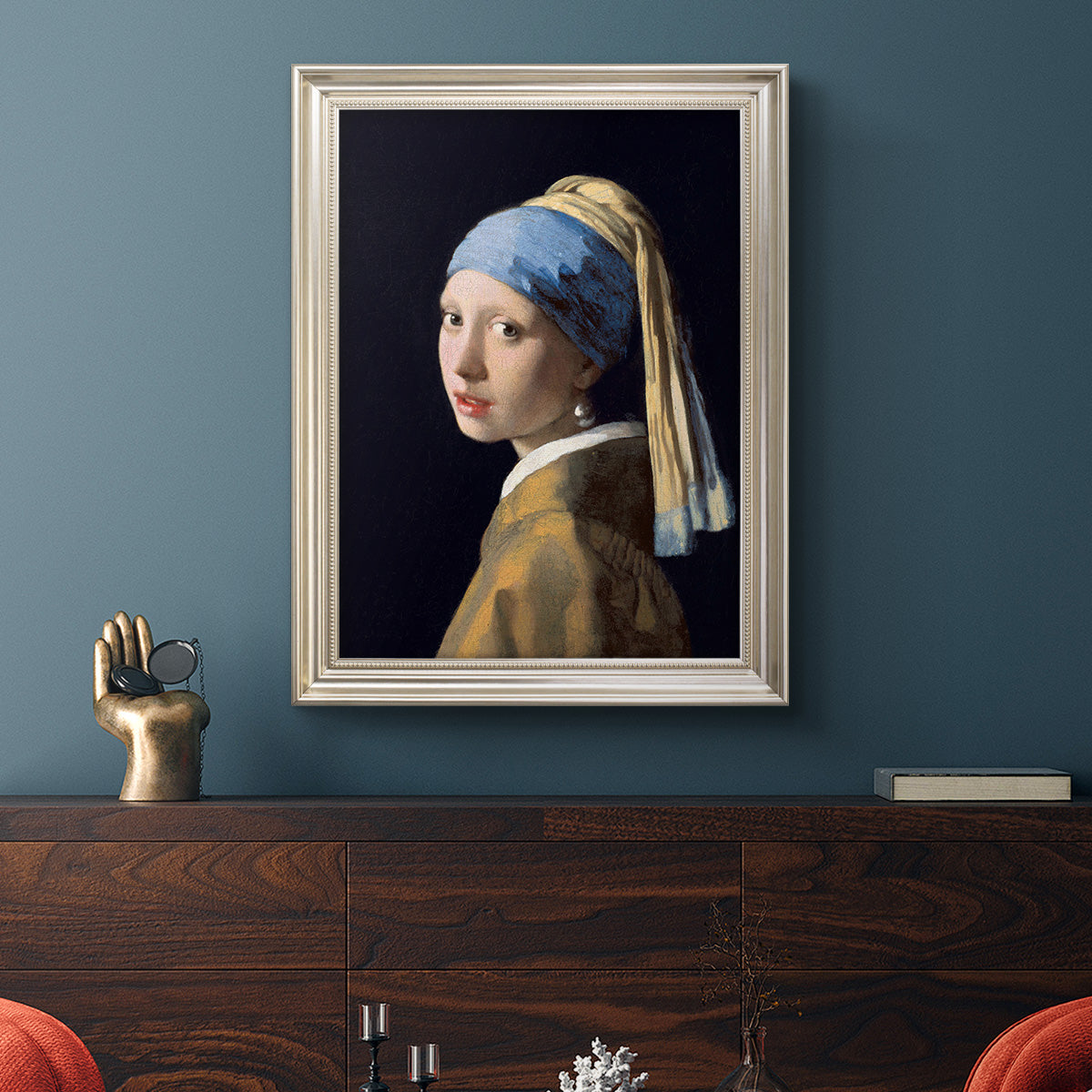 Iconic portrait of a girl wearing a pearl earring by Johannes Vermeer in an ornate champagne frame displayed in a dark-toned interior setting.