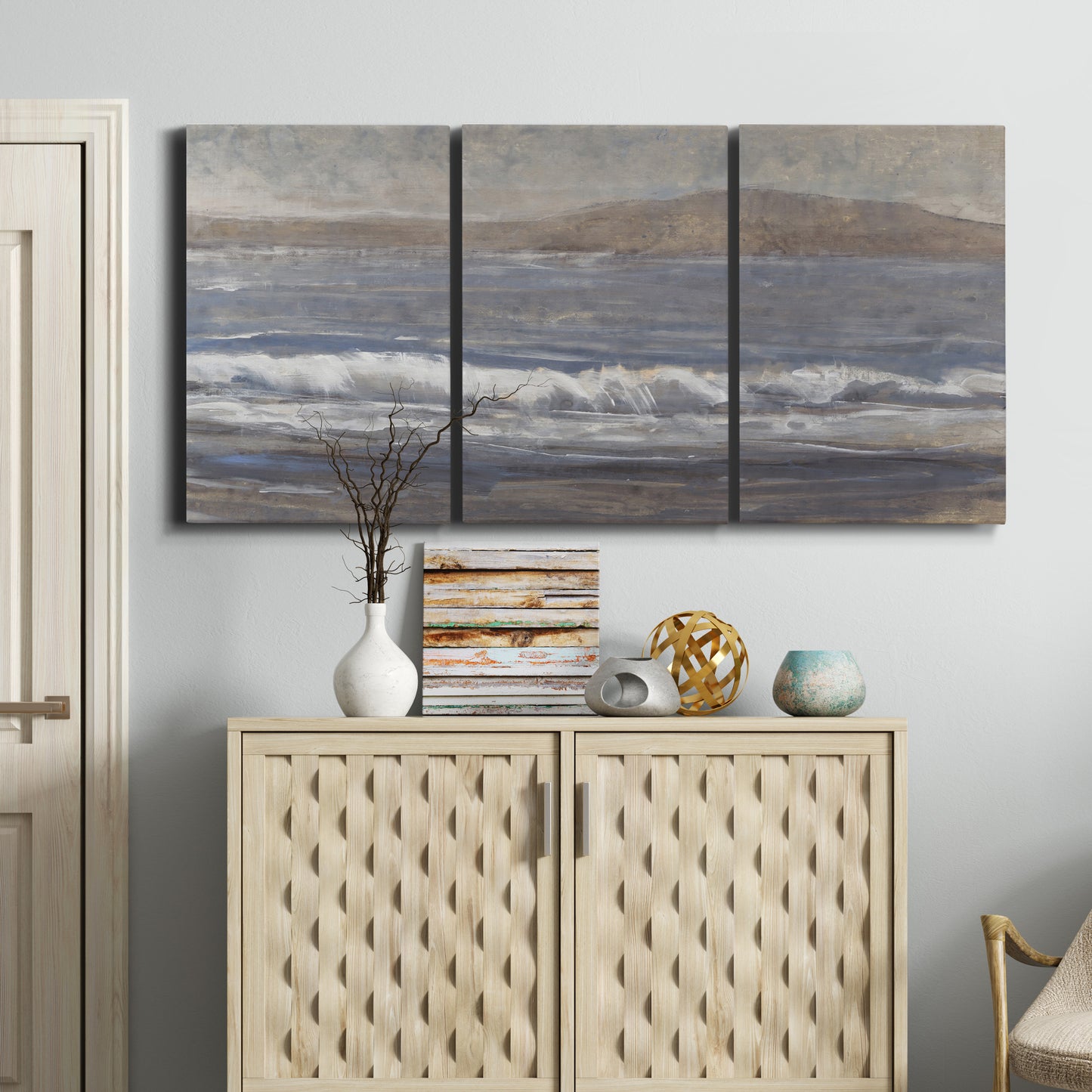Three-panel canvas wall art featuring shoreline between land and sea, displayed above a cabinet in an entryway.
