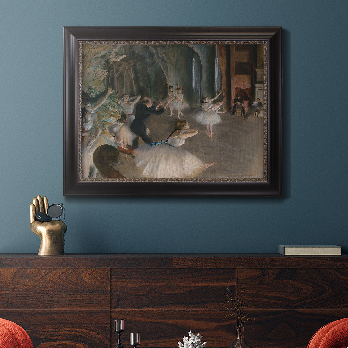 Impressionist backstage ballet scene by Edgar Degas in an ornate black frame with gilded inner detail displayed in a dark-toned interior setting.
