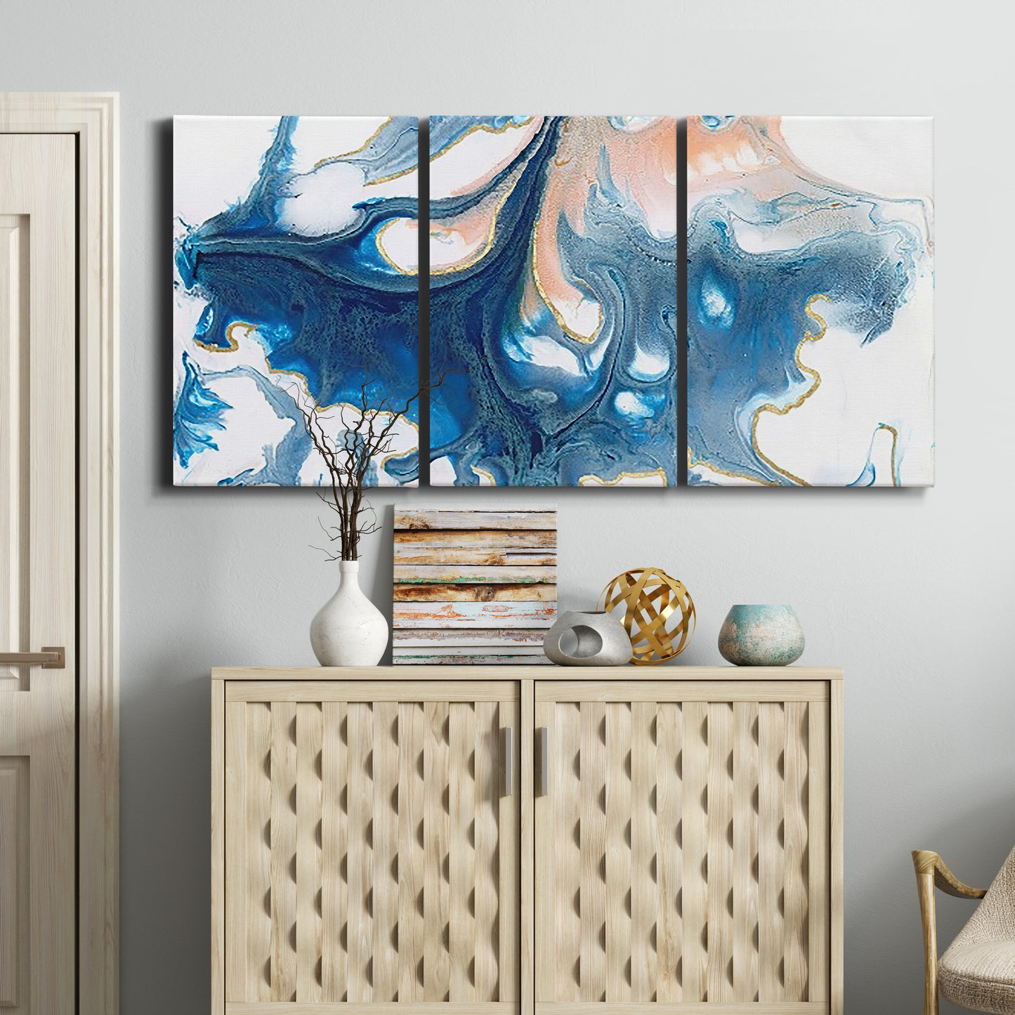 Three-panel canvas wall art featuring flowing blue abstract movement, displayed above a cabinet in an entryway.