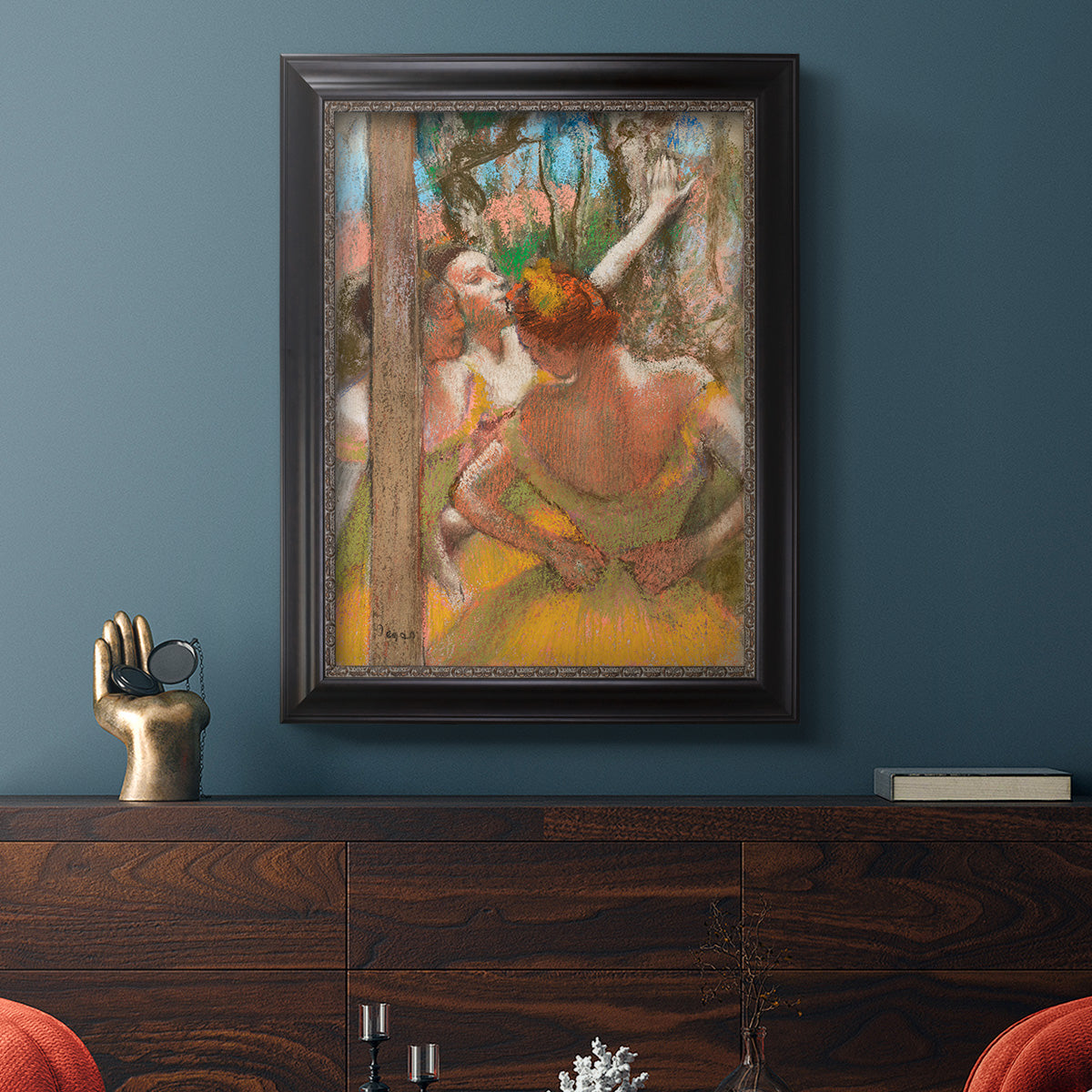 Impressionist ballet dancer composition by Edgar Degas in an ornate black frame with gilded inner detail displayed in a dark-toned interior setting.