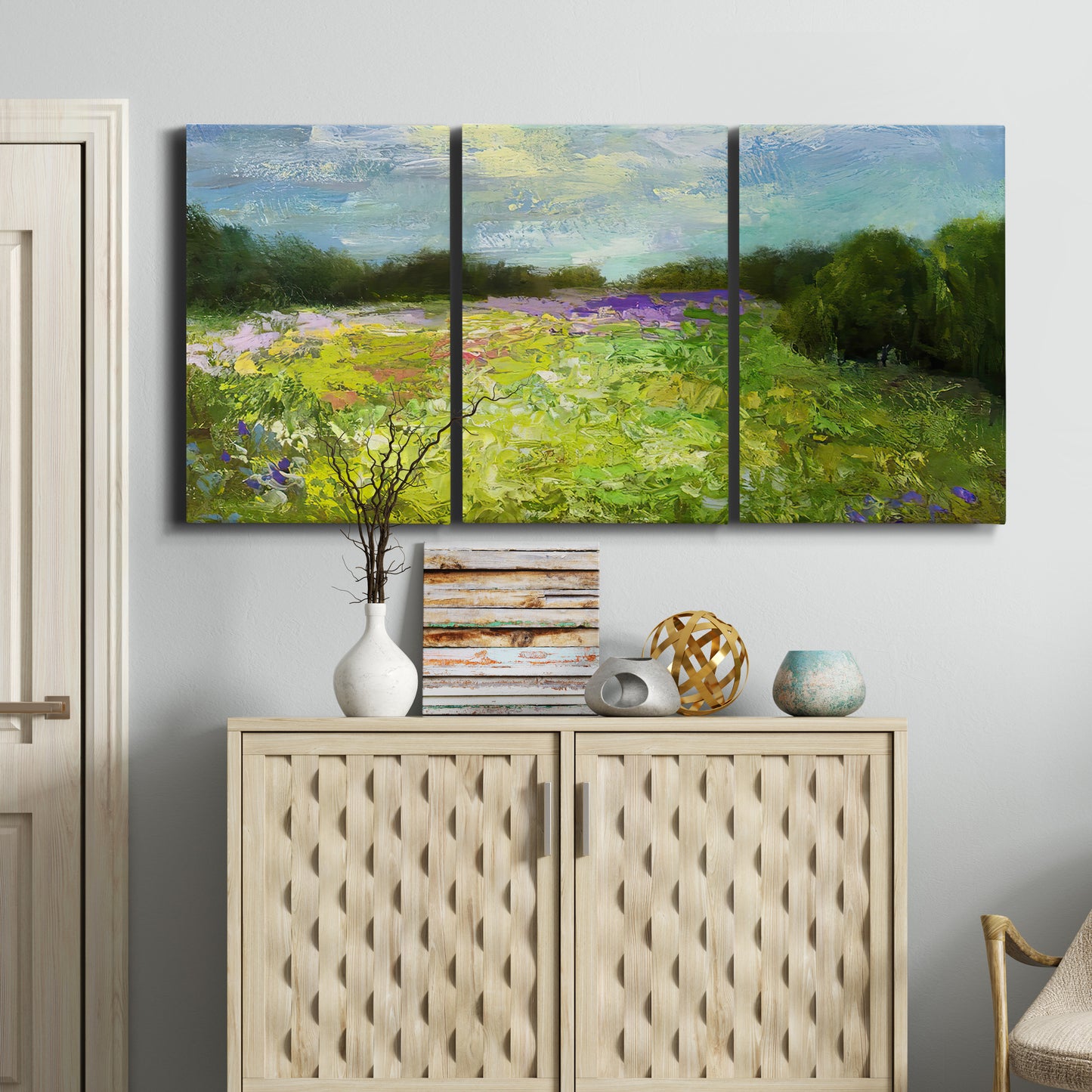 Three-panel canvas wall art featuring pastoral field with wildflowers, displayed above a cabinet in an entryway.