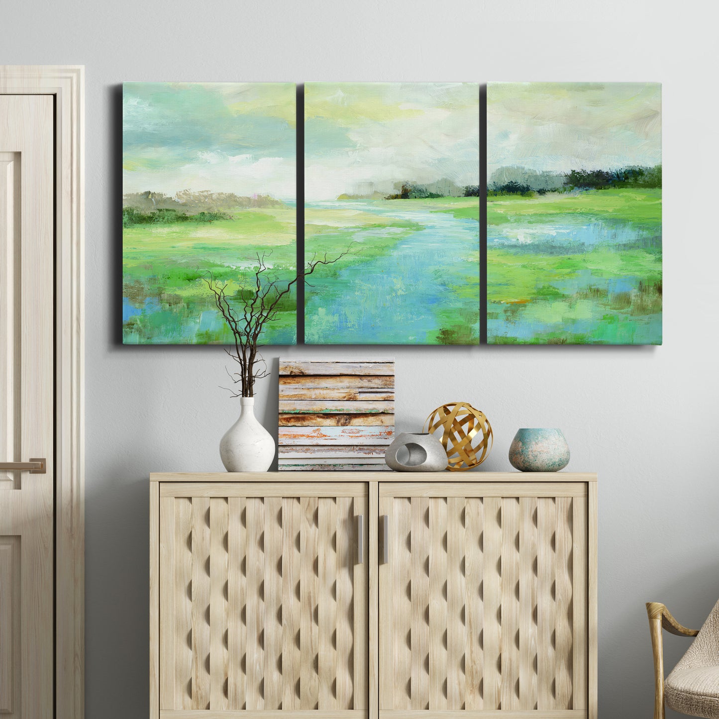 Three-panel canvas wall art featuring gentle stream winding through trees, displayed above a cabinet in an entryway.