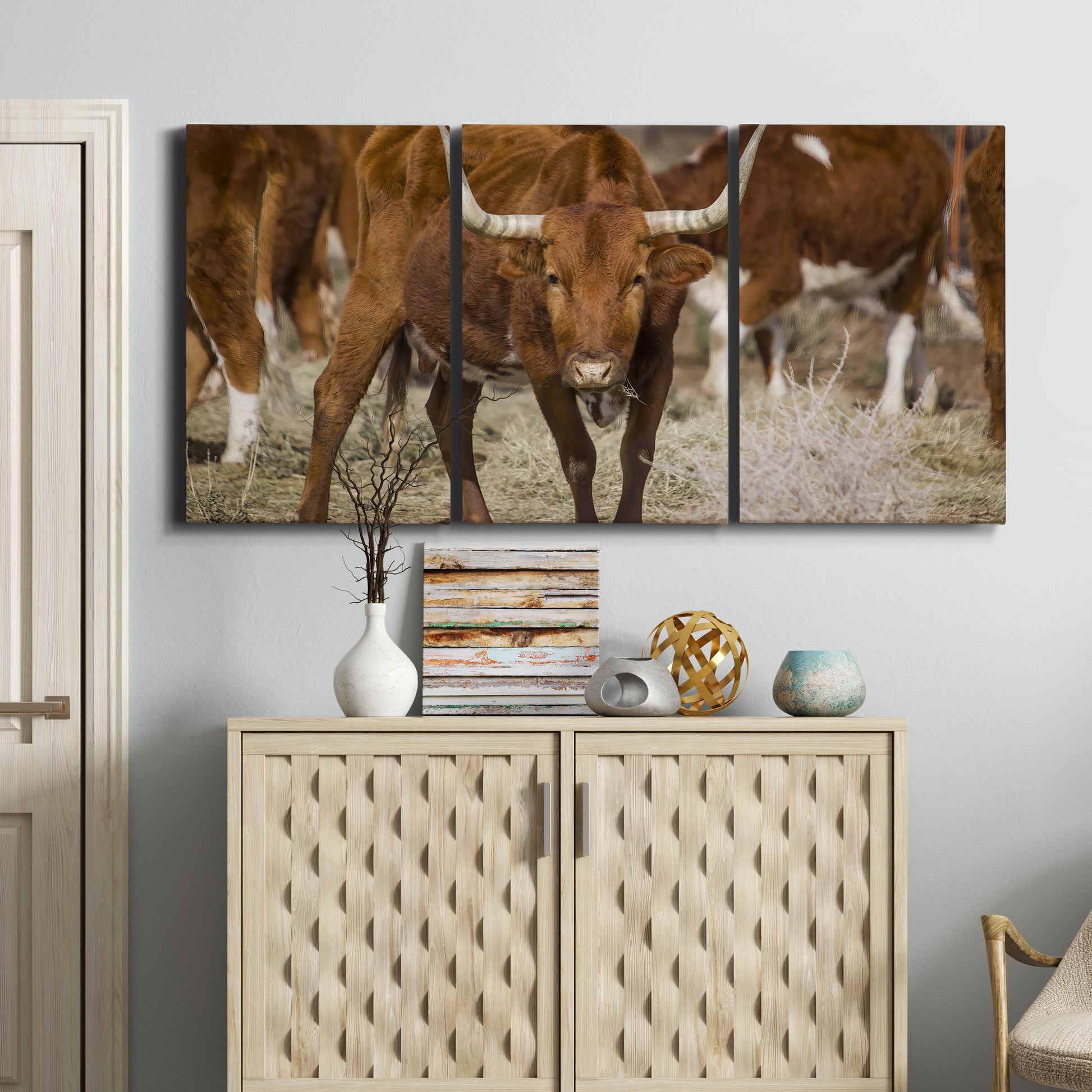 Three-panel canvas wall art featuring longhorn cattle standing together, displayed above a cabinet in an entryway.
