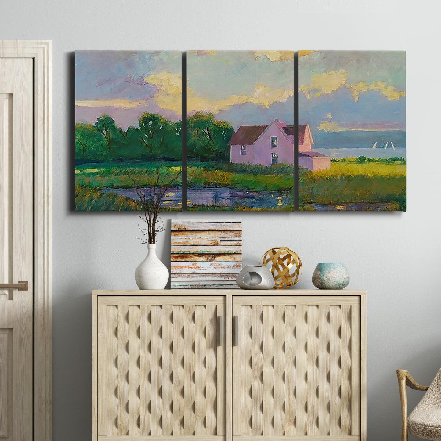 Three-panel canvas wall art featuring farmhouse near coastline landscape, displayed above a cabinet in an entryway.