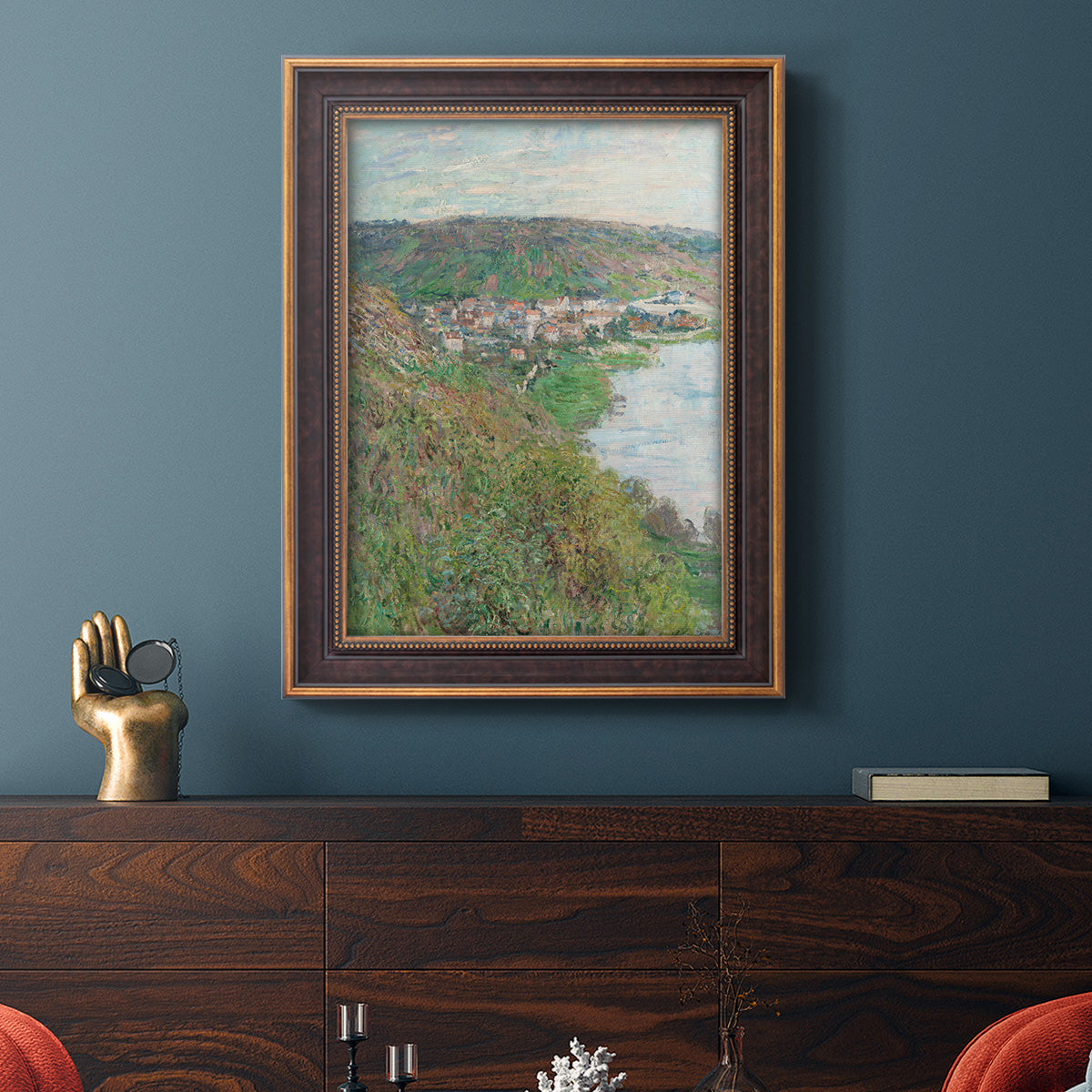 Impressionist landscape view of Vétheuil by Claude Monet in an ornate bronzed mahogany wood frame displayed in a dark-toned interior setting.