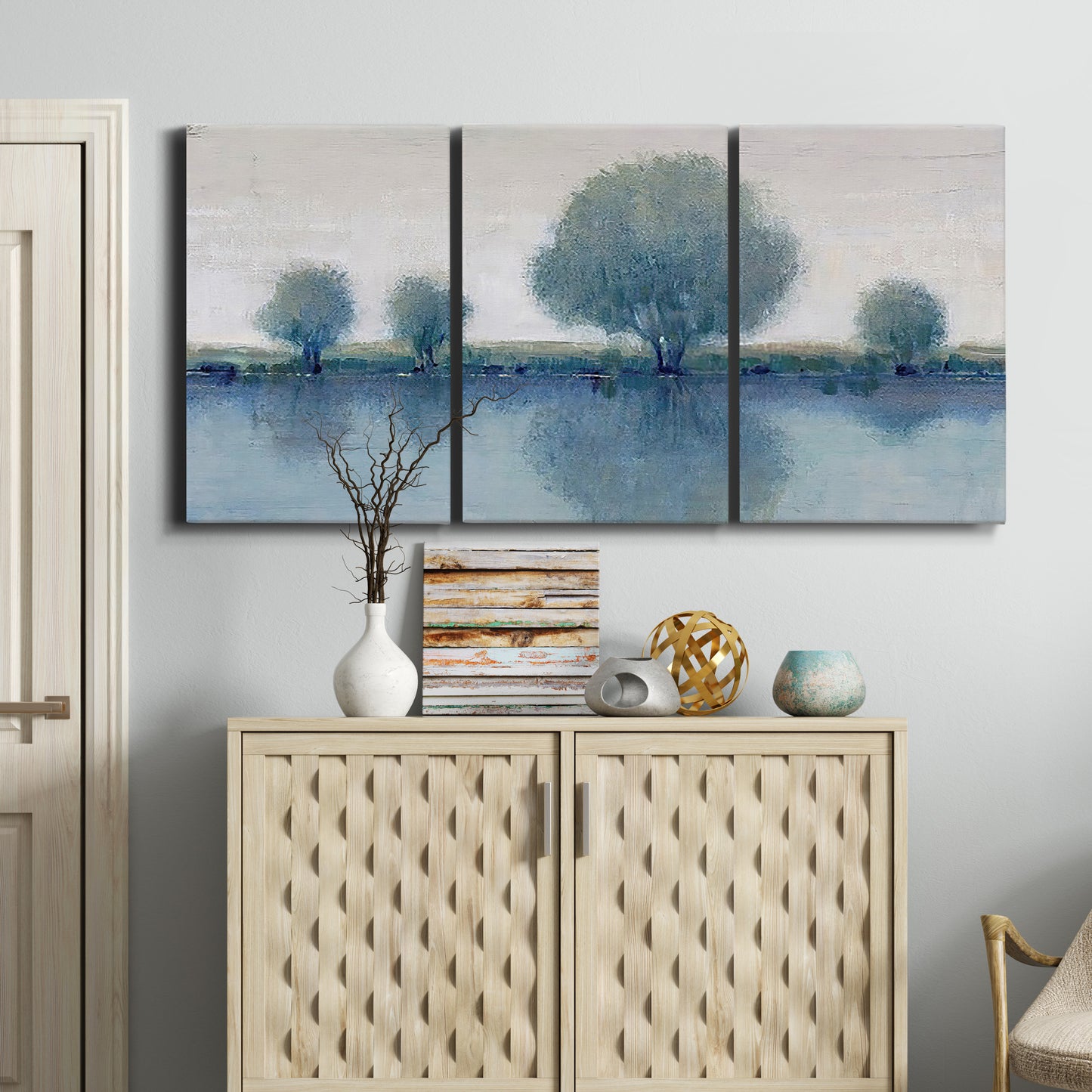 Three-panel canvas wall art featuring calm afternoon river reflection, displayed above a cabinet in an entryway.