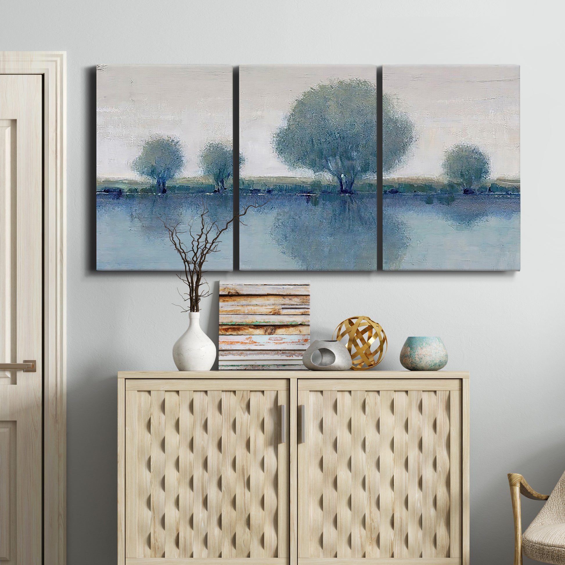 Three-panel canvas wall art featuring calm afternoon river reflection, displayed above a cabinet in an entryway.