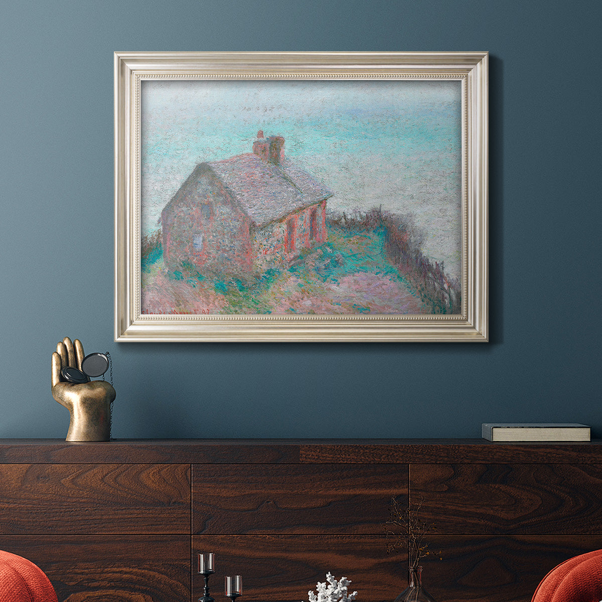 Impressionist coastal building landscape by Claude Monet in an ornate champagne frame displayed in a dark-toned interior setting.