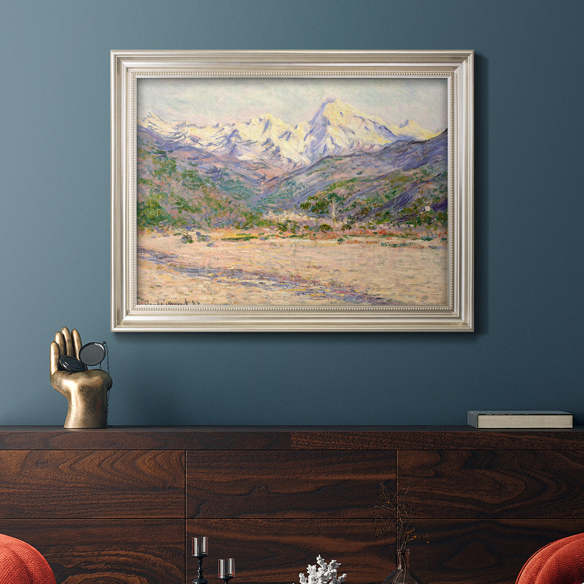 Impressionist valley landscape in southern France by Claude Monet in an ornate champagne frame displayed in a dark-toned interior setting.