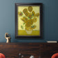 Impressionist sunflower still life painting by Vincent van Gogh in an ornate black frame with gilded inner detail displayed in a dark-toned interior setting.