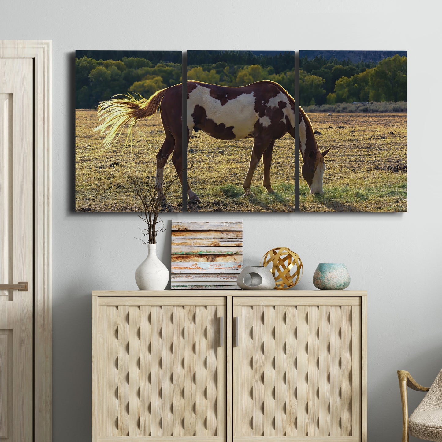 Three-panel canvas wall art featuring horses standing near farmhouse, displayed above a cabinet in an entryway.