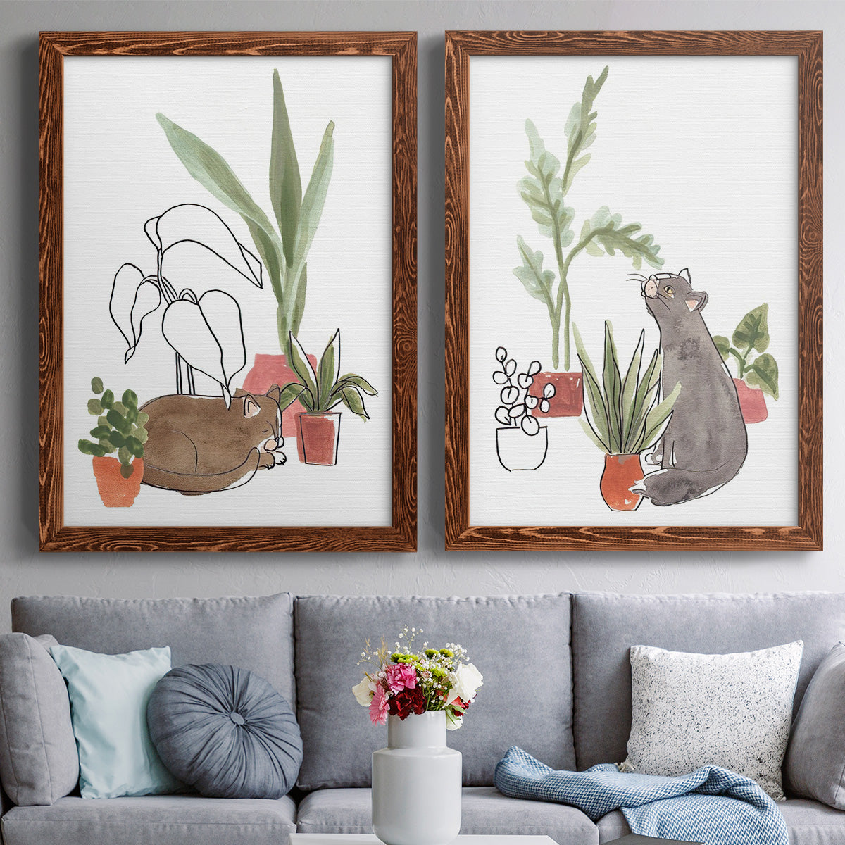 Set of two maple barnwood framed canvas prints depicting paired whimsical botanical animal illustrations with curious felines, terracotta pots, succulents, and leafy stems above a sofa in a contemporary living room.