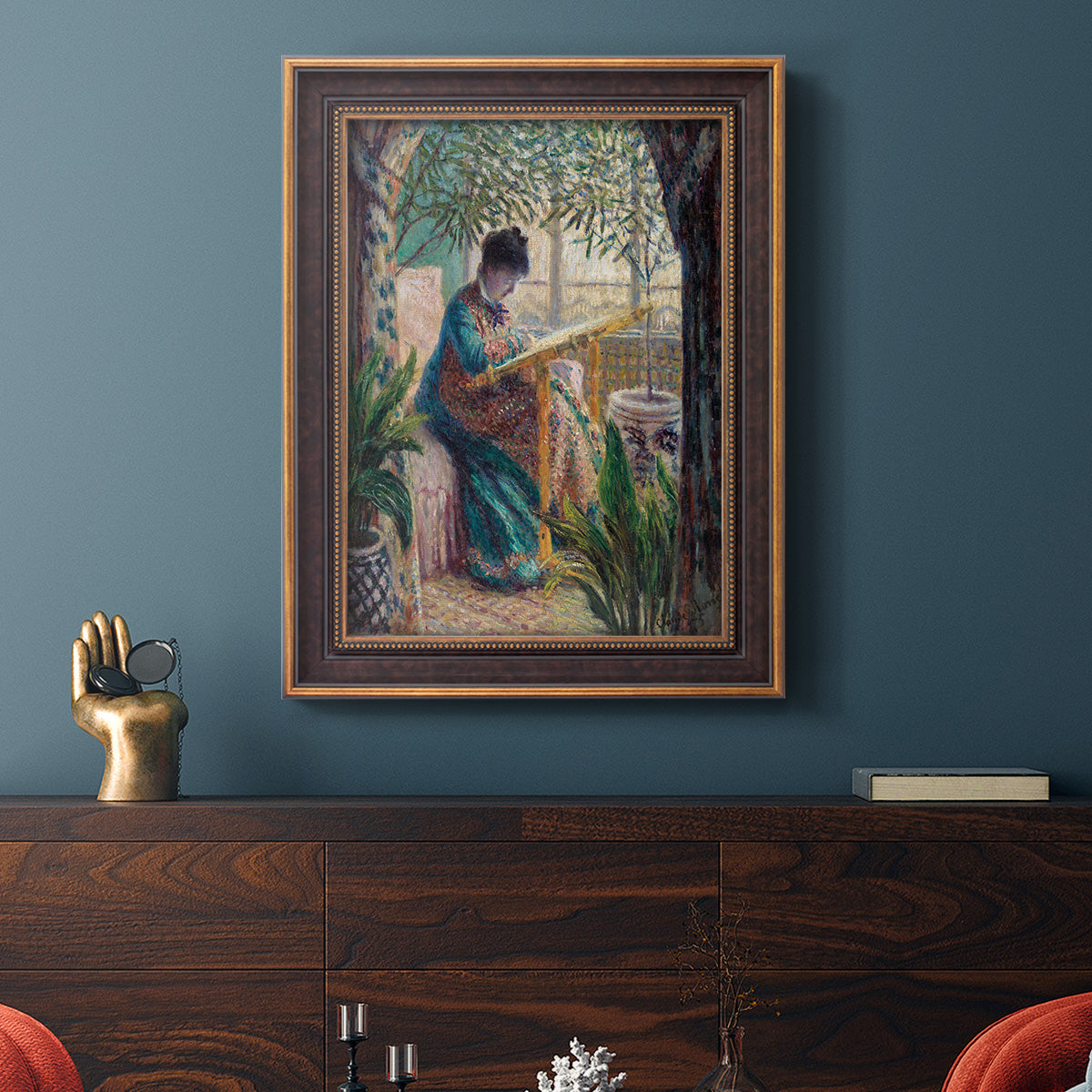 Impressionist portrait of Madame Monet sewing by Claude Monet in an ornate bronzed mahogany wood frame displayed in a dark-toned interior setting.