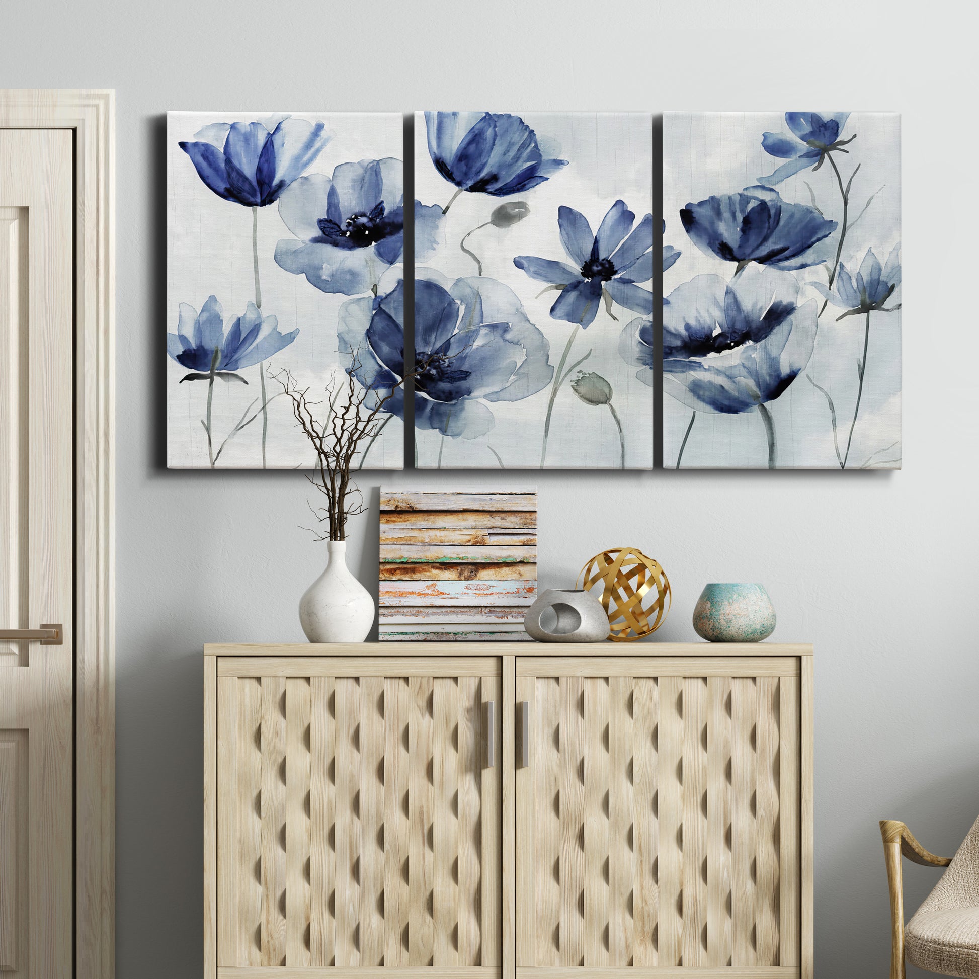 Three-panel canvas wall art featuring indigo floral blossoms awakening, displayed above a cabinet in an entryway.