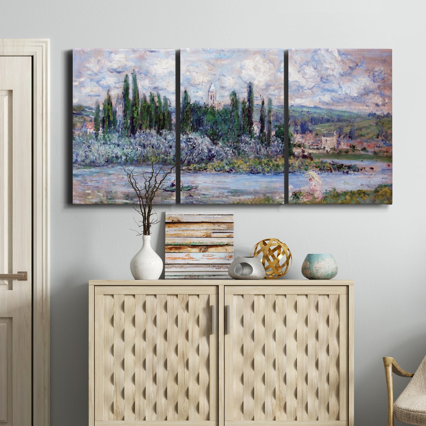 Three-panel canvas wall art featuring summer village view along river, displayed above a cabinet in an entryway.