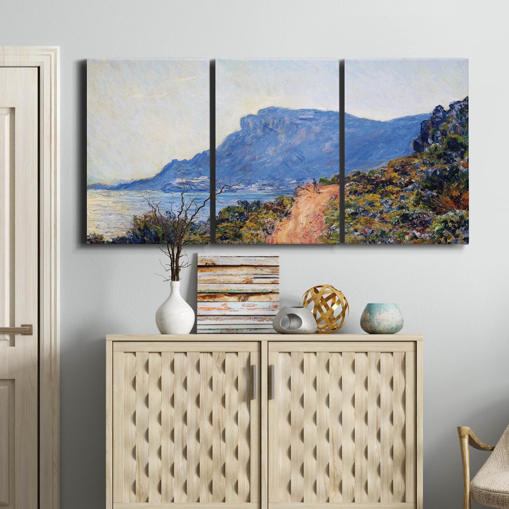 Three-panel canvas wall art featuring winding coastal road above sea, displayed above a cabinet in an entryway.