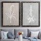 Set of two black barnwood framed canvas prints depicting paired rustic minimalist botanical prints with delicate stems, leaves, and blossoms against gray taupe and pale blue panels above a sofa in a contemporary living room.