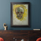 Expressive skull study painting by Vincent van Gogh in an ornate black frame with gilded inner detail displayed in a dark-toned interior setting.