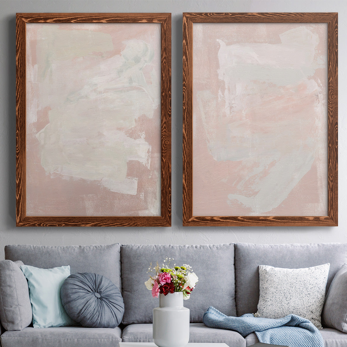 Set of two maple barnwood framed canvas prints depicting paired minimalist color-field abstracts with cloudy rose washes, broad pale strokes, and subtle texture above a sofa in a contemporary living room.