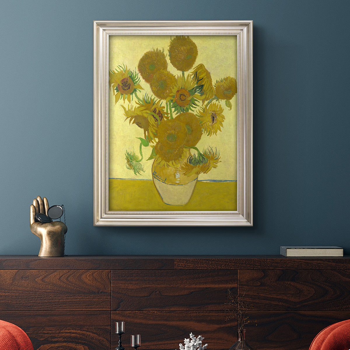 Impressionist sunflower still life painting by Vincent van Gogh in an ornate champagne frame displayed in a dark-toned interior setting.
