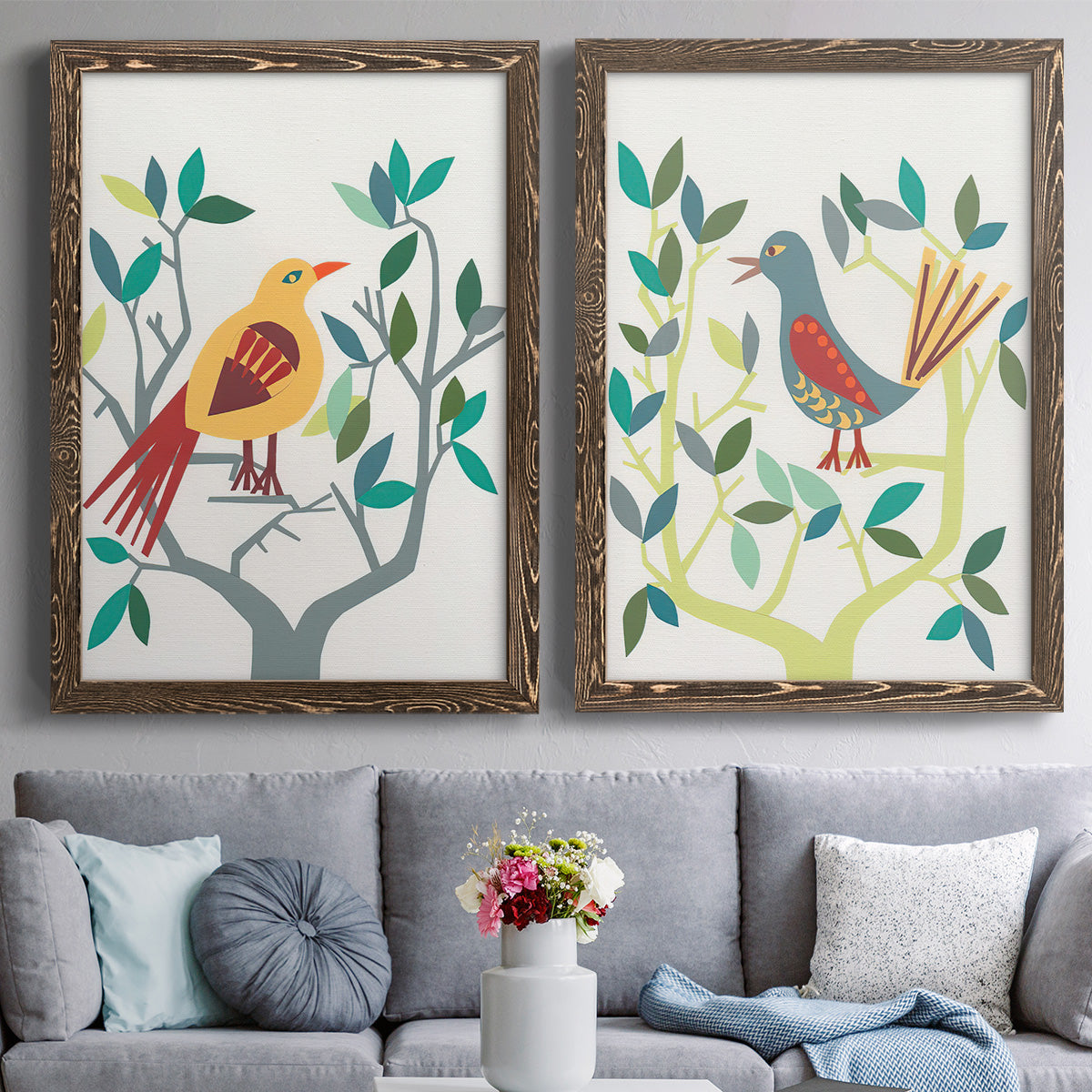 Set of two walnut barnwood framed canvas prints depicting paired modern folk-art bird illustrations with red yellow blue plumage, simplified leaves, and playful flat shapes above a sofa in a contemporary living room.