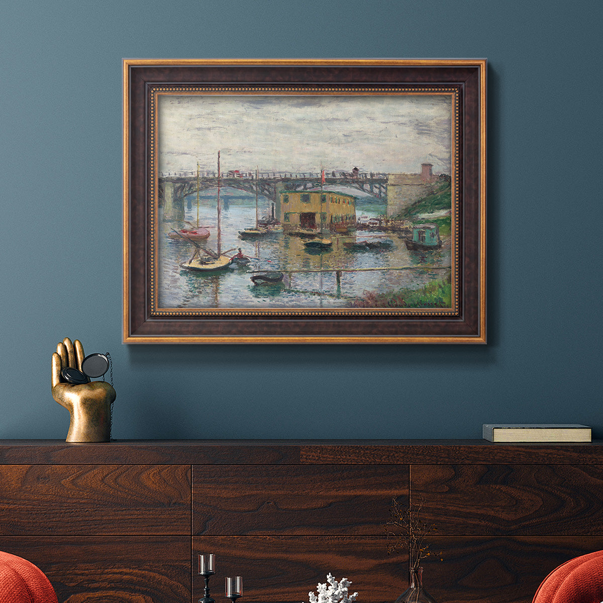 Impressionist river bridge scene on an overcast day by Claude Monet in an ornate bronzed mahogany wood frame displayed in a dark-toned interior setting.