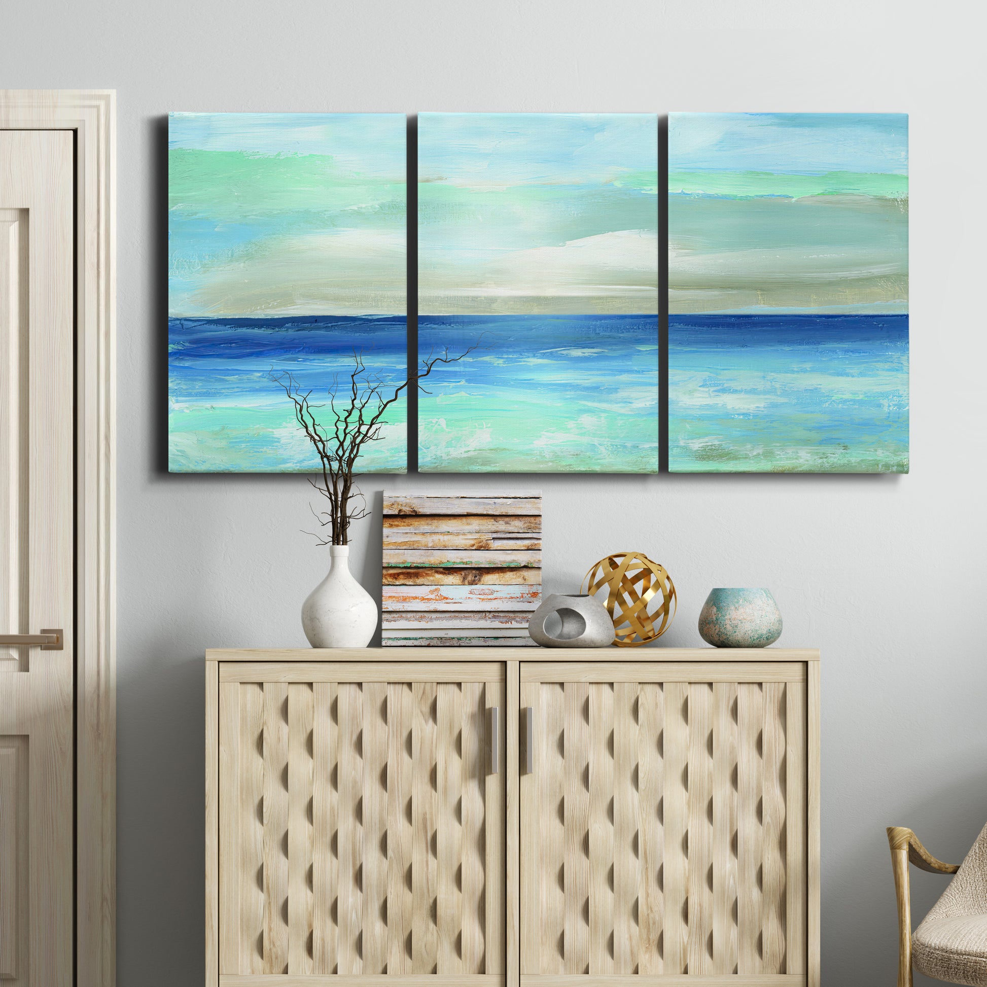 Three-panel canvas wall art featuring vast open blue ocean horizon, displayed above a cabinet in an entryway.