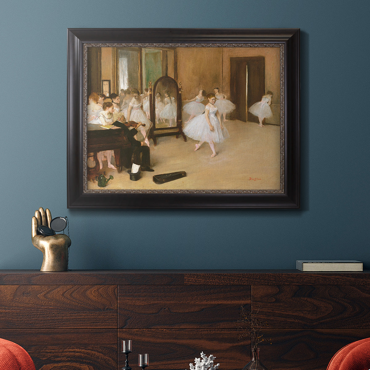 Impressionist dance class interior scene by Edgar Degas in an ornate black frame with gilded inner detail displayed in a dark-toned interior setting.