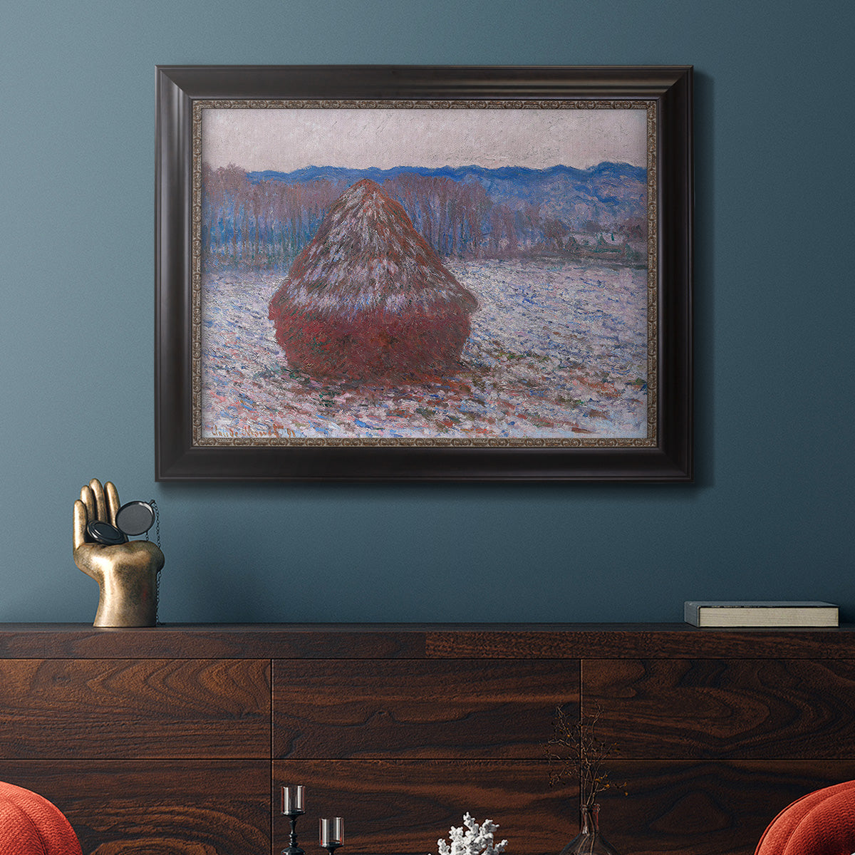 Impressionist single haystack landscape by Claude Monet in an ornate black frame with gilded inner detail displayed in a dark-toned interior setting.