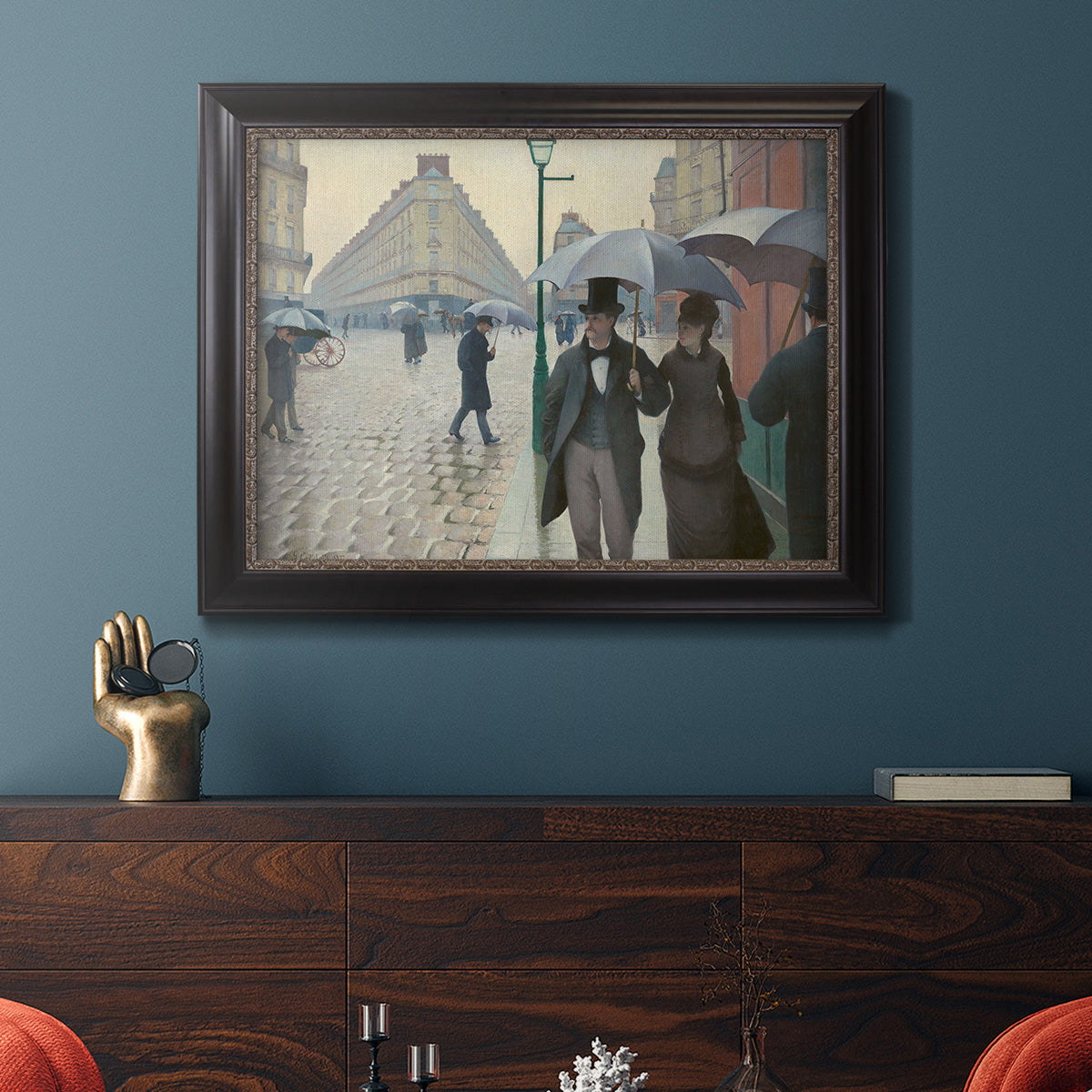 Impressionist urban street scene in the rain by Gustave Caillebotte in an ornate black frame with gilded inner detail displayed in a dark-toned interior setting.