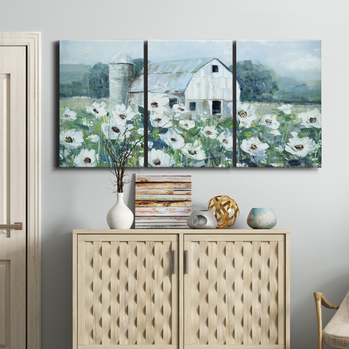Three-panel canvas wall art featuring pastoral farmland with open fields, displayed above a cabinet in an entryway.