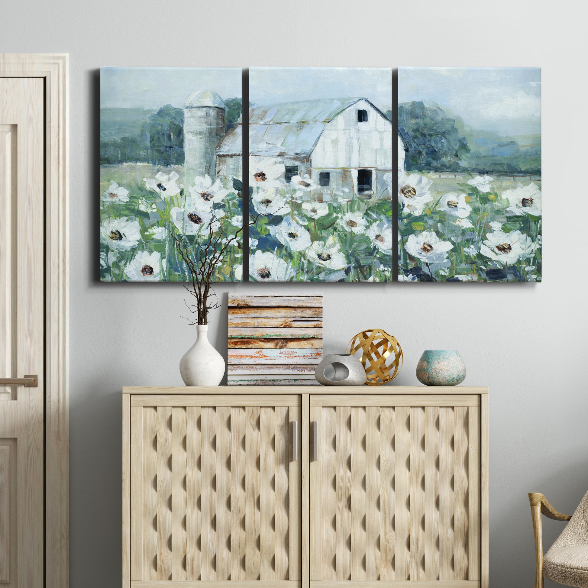 Three-panel canvas wall art featuring pastoral farmland with open fields, displayed above a cabinet in an entryway.