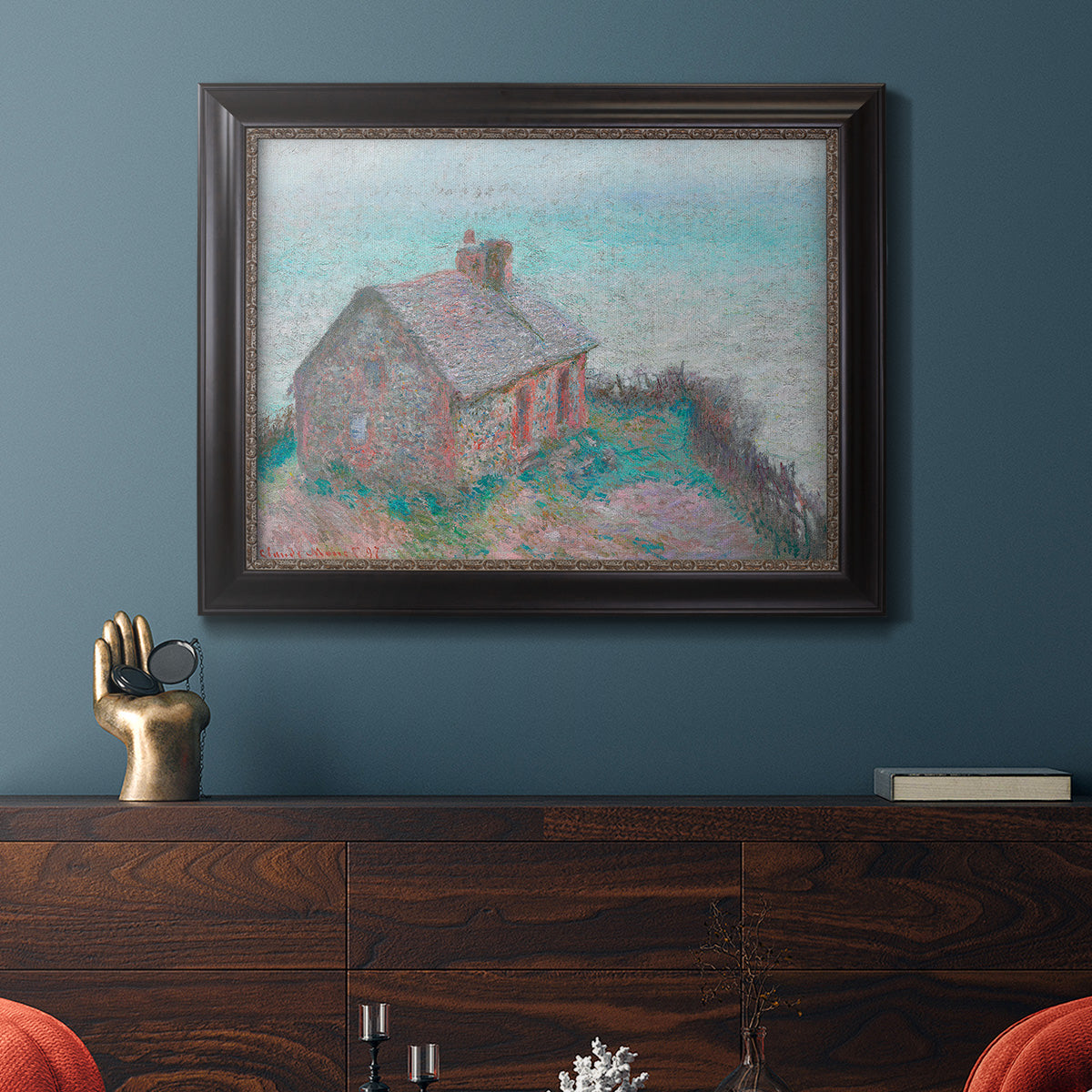 Impressionist coastal building landscape by Claude Monet in an ornate black frame with gilded inner detail displayed in a dark-toned interior setting.